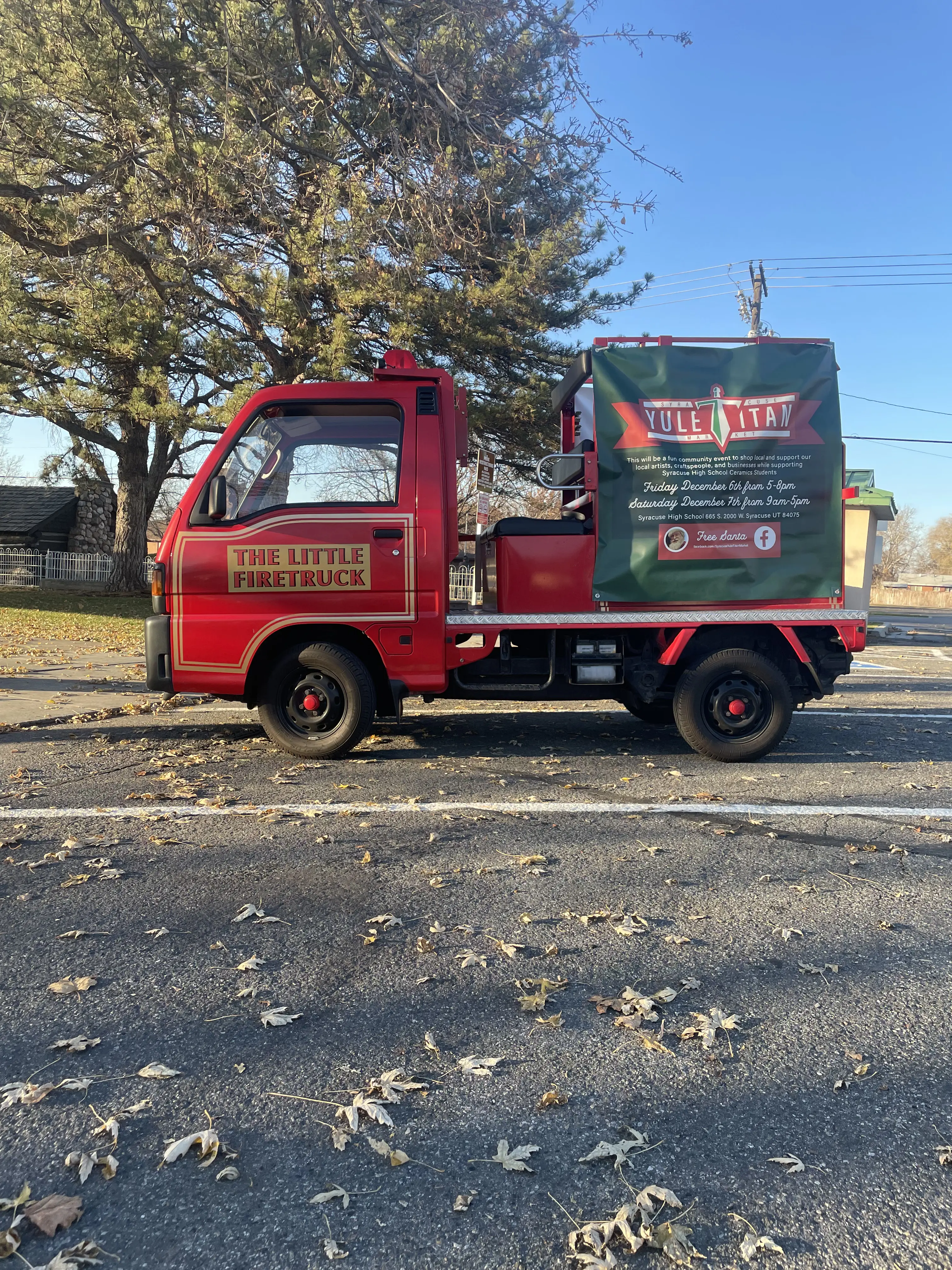 The Little Red Japanese Firetruck with a Banner for a Market on the side with a park in the background.